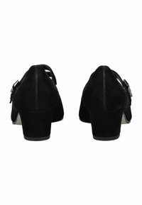 Zapatos de tacón de ante negro con punta redonda y tacón bajo apilado. Presentan un detalle de hebilla en el lateral y una superficie lisa y texturizada.