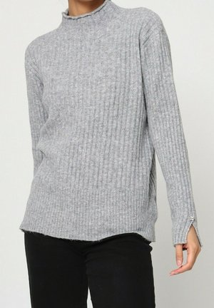 Pull en gris à côtes avec un col montant, des manches longues et un ourlet légèrement court. Présente des fentes sur les côtés et un tissu texturé.