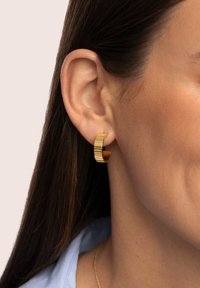 Pendiente de aro dorado con textura acanalada, que presenta un interior liso y un diseño angular, usado en el lóbulo de la oreja.