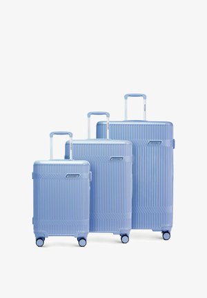 Drie lichtblauwe koffers met harde schaal in kleine, middelgrote en grote maat, elk voorzien van een telescopisch handvat en vier wielen, naast elkaar geplaatst.