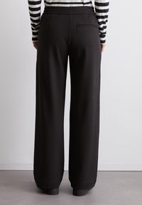 Zwarte wijde broek met een elastische tailleband. Heeft een enkele achterzak en een gladde stoftextuur.