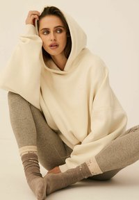 Kremowy, oversize'owy hoodie z kapturem, zestawiony z teksturowanymi, szarymi leginsami i brązowymi skarpetkami z delikatnym wzorem pasków.