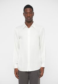 Hvit langermet skjorte med vertikale striper, knappelukking foran og en skarp krage. Laget av lett, glatt stoff med en avslappet passform.