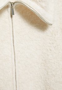Mikina na zip z fleece v off-white barvě, s měkkou texturou a stříbrným zapínáním na přední straně. Čisté linie a žádné další vzory.