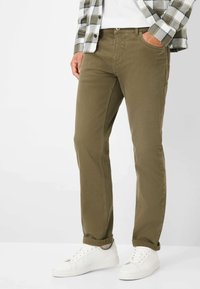 Pantaloni khaki in cotone con design a gamba dritta, dotati di tasche laterali e una texture liscia. Abbinati a sneaker bianche.