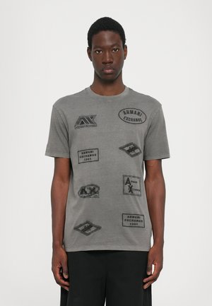 Tricou gri din bumbac cu mai multe patch-uri grafice negre și logo-uri, inclusiv "Armani Exchange" și detalii cu modele pe întreaga suprafață.