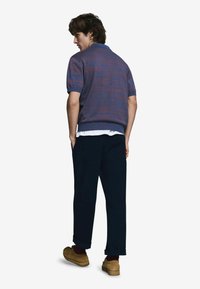 Polokošeľa s krátkym rukávom v odtieňoch fialovej a modrej, pletená textúrovaná tkanina, čierne nohavice a béžové dreváky. Má golier a jemný vzor.