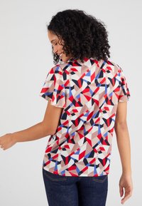 Korte mouw top gemaakt van lichtgewicht stof met een geometrisch patroon in rood, blauw en beige, met een ontspannen pasvorm en een gebogen zoom.