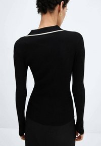 Suéter negro de manga larga con canalé, que presenta un borde en color blanco y un diseño ajustado, confeccionado en un tejido suave y texturizado.