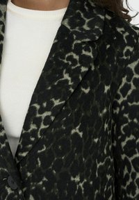 Blazer leopard-print nero e crema in un morbido tessuto testurizzato con collo a laccio e chiusura frontale con un bottone.