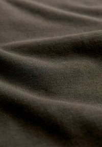 Gros plan sur un tissu doux de couleur brun foncé montrant une texture fine en maille et des plis délicats créant des ombres subtiles.