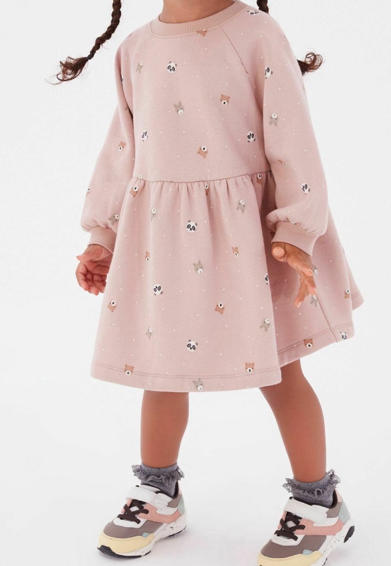 Ein Kind trägt ein pinkes Kleid mit Tiermotiven, das gepuffte Ärmel und einen ausgestellten Rock hat, kombiniert mit bunten Turnschuhen und grauen Socken.