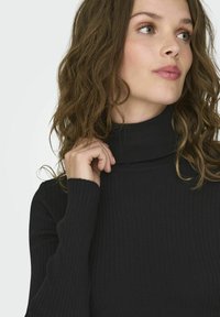 Maglione nero a coste con colletto alto e maniche lunghe aderenti, caratterizzato da una texture morbida e un design che abbraccia il corpo.