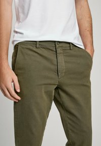 Pantalones de algodón verde oliva con corte recto, que cuentan con cierre frontal de cremallera y botón, y bolsillos laterales inclinados. Textura suave.