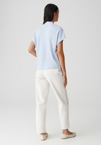 Haut en tricot bleu clair à manches courtes, texture douce. Associé à un pantalon droit blanc et des chaussures plates légères. Design simple et épuré.