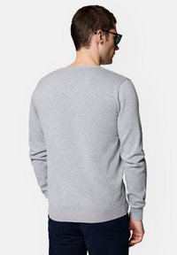 Szary sweter z okrągłym dekoltem i długimi rękawami, z prążkowanymi mankietami i dołem, wykonany z miękkiej dzianiny, widziany z tyłu, noszony z ciemnymi spodniami.