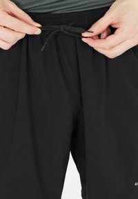 Sorte sportsshorts med elastisk livrem, snøre til justering og glat tekstur. Brandlogo synligt på siden.
