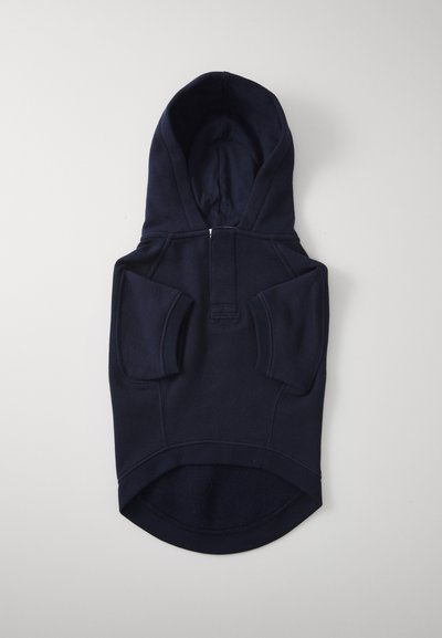 Laivastonsininen koirantakki hupulla, lyhyillä hihoilla, vetoketjulla edessä ja kaarevalla alareunalla vaaleanharmaalla taustalla.