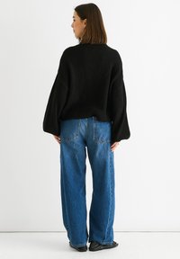 Maglione nero oversize con orlo a coste, abbinato a jeans a gamba ampia blu a vita alta. Tessuto liscio con una vestibilità leggermente rilassata.