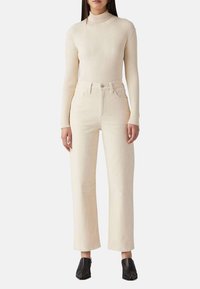 Un haut à col roulé beige côtelé à manches longues associé à un jean large taille haute crème, complété par des chaussures noires à enfiler.