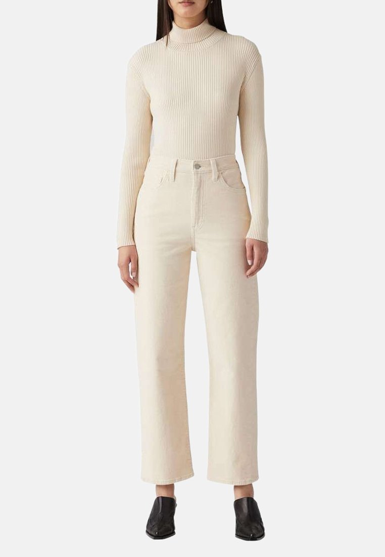 Un haut à col roulé beige côtelé à manches longues associé à un jean large taille haute crème, complété par des chaussures noires à enfiler.