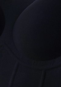 Reggiseno nero con coppe lisce, imbottite e design senza cuciture. Presenta una texture di tessuto morbido e un'estetica minimalista.