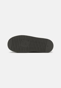 Semelle de chaussure en caoutchouc noir avec des nervures texturées, bout arrondi et logo carré en relief. Bord légèrement surélevé pour une meilleure adhérence. Taille indiquée comme 37.