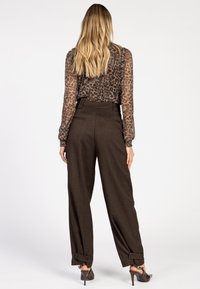 Doorzichtig blouse met luipaardprint, gecombineerd met hoge, bruine geruite broek. De broek heeft omslagen en twee achterzakken.