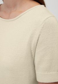 Top in maglia crema con scollatura rotonda e maniche corte. Presenta un motivo testurizzato e polsini a coste. Tessuto morbido con un aspetto leggero.