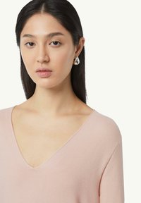 Light pink V-neck sweater with ribbed texture, paired with silver teardrop earrings. Model's hair is straight and dark.