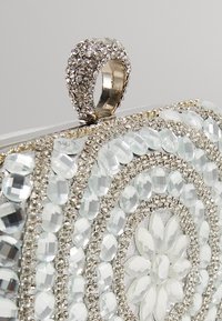 Pochette à perles avec un motif floral, une quincaillerie ton argent et une surface texturée. Présente des accents clairs et en miroir.