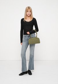 Grønn semsket håndveske med en strukturert design og to topphåndtak, kombinert med en svart langermet topp og lyseblå vide jeans.