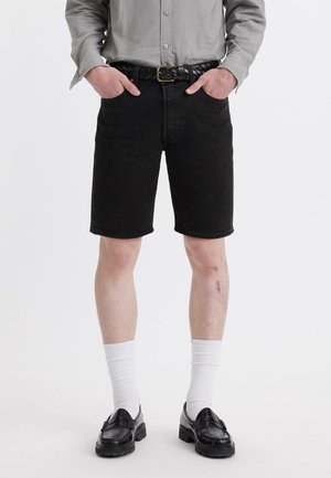 Black denim shorts with a straight cut, worn with a grey long-sleeve shirt, black braided belt, white socks, and black loafers.