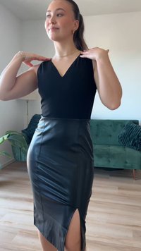 Vestido preto sem mangas com decote em V, feito de material semelhante a couro. Apresenta uma fenda alta no lado esquerdo, silhueta ajustada e textura suave.