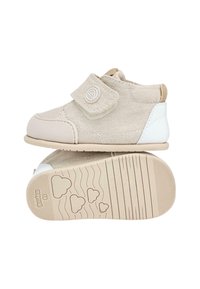 Botas de tobillo de lienzo beige con una correa de velcro y tacón blanco. Suela suave con patrones de huella en forma de corazón. Textura lisa, diseño informal.