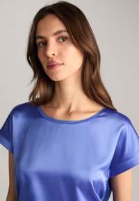 Satijnen blauwe top met een ronde halslijn en korte mouwen, met een gladde textuur en subtiele glans. Geen patronen of hardware zichtbaar.