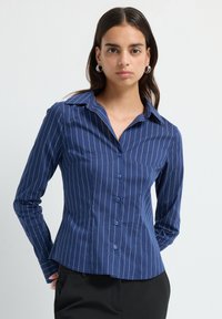 Camicia a bottoni blu navy realizzata in tessuto misto cotone, con strisce verticali bianche, colletto a punta e silhouette aderente.