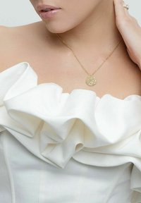 Guldig halsband med en texturerad rund pendant, bärs med en vit utan axelbands topp med framträdande volanger och slät tyg.