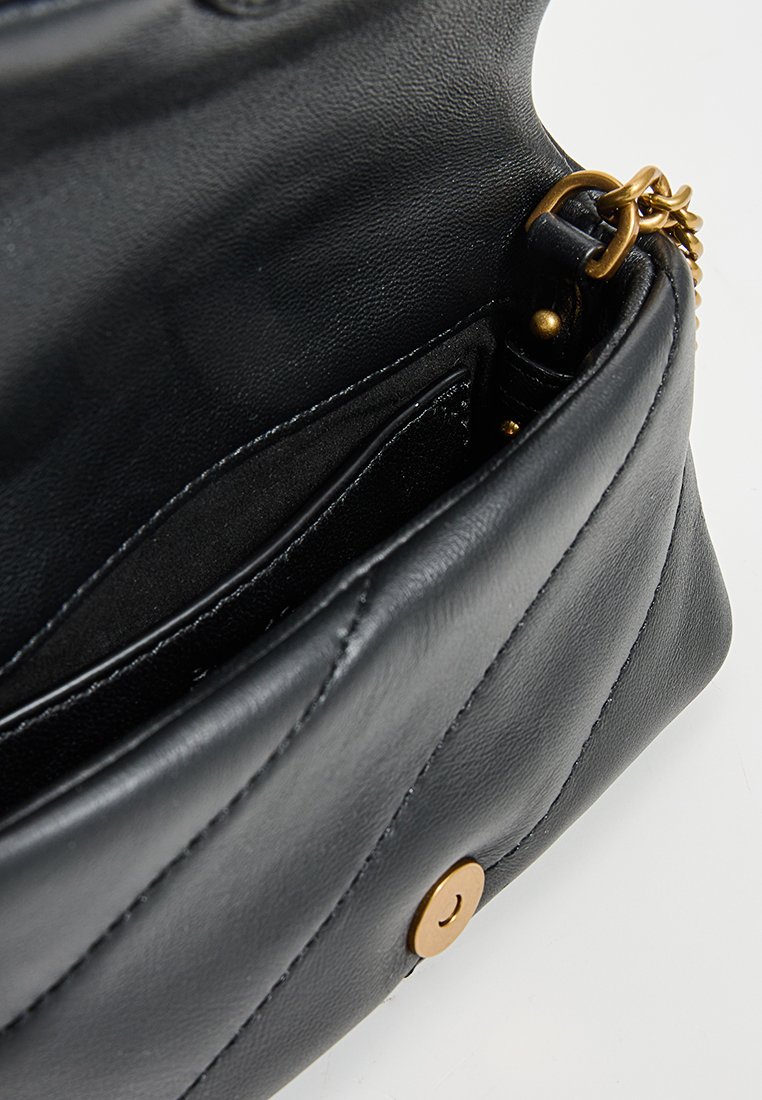 Intérieur d'un sac en cuir noir avec une texture lisse, doté d'une fermeture à pression en métal doré et de plusieurs poches de rangement.
