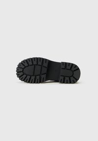 Suela de goma negra con surcos profundos para tracción, con una superficie texturada y una forma de punta redondeada. Ideal para su uso al aire libre.