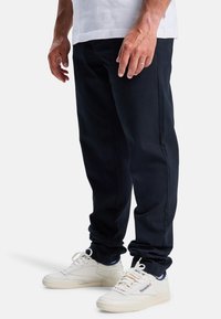 Navy blauwe katoenbroek met een rechte pijp, gecombineerd met witte leren sneakers met blauwe accenten en platte veters.