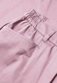 Pantalon rose avec une taille froncée, comportant une poche latérale et une texture lisse, mettant en avant des détails de couture simples.