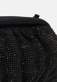 Musta paljettilaukku, jossa on teksturoitu pinta ja pehmeä musta kangassuljin. Muotoilu on pyöreä ja siinä on kerroskankaisia yksityiskohtia.