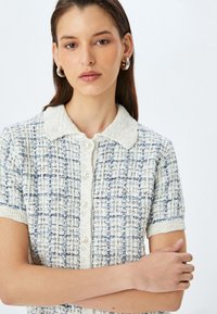 Genaaid polo sweater met korte mouwen in crème en lichtblauw, met een geweven structuur, een knoopsluiting aan de voorkant en een zachte, contrasterende kraag.