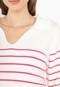 Pull blanc à rayures horizontales roses, avec un col en V et un col. Un fin collier en or avec un petit pendentif est visible.