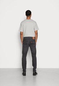 Camiseta de cuello redondo gris claro combinada con jeans negros que cuentan con una etiqueta de cuero, ajuste slim y bolsillos traseros clásicos. Zapatos negros completan el look.