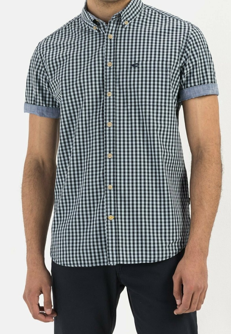 Camicia a maniche corte con bottoni in un motivo a scacchi bianco e nero, con accenti in denim blu chiaro alle maniche. Presenta una tasca sul petto e bottoni in legno.