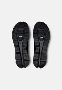 Semelles de chaussures de sport noires avec un caoutchouc texturé, présentant des crampons multidirectionnels et un accent bleu clair au centre.