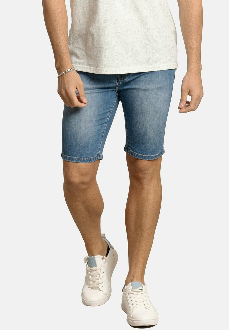 Pantalones cortos de mezclilla en azul claro con dobladillos enrollados, con un ajuste clásico. Combinados con zapatillas blancas, presentan un aspecto limpio y casual.