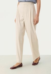 Light beige tailored pants with pleats and a straight-leg design, paired with maroon flats featuring a glossy finish and minimal detailing.